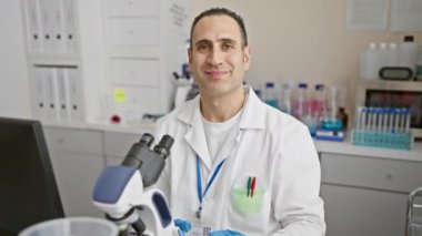 Neşeli galibiyet! Bilim adamı üniformalı genç İspanyol adam laboratuardaki başarısını kutluyor. Kendine güvenen zafer ifadesi ve neşeli bir gülümseme sergiliyor.