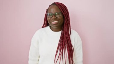 Gözlüklü ve pembe arka planda beyaz kazaklı, gülümseyen siyah kadın.