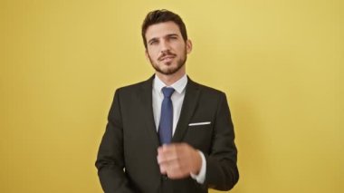 Yakışıklı, takım elbiseli, pozitif ışıldayan, kendine güvenen, elinde çenesi ve kollarını kavuşturmuş genç bir adam. Direk kameraya bakıyor, neşeli sarı arka planda tek başına dikiliyor.