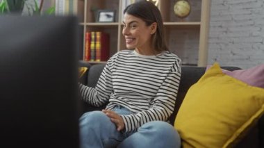 Neşeli bir İspanyol kadın evinde bir koltukta oturuyor, elinde bir hediye, mutluluk ve beklenti ifade ediyor..