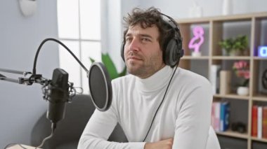 Sinirli genç İspanyol adam, stres ve endişe içinde tırnaklarını yiyor, radyo stüdyosunda korkmuş görünüyor, kulaklıklar açık.