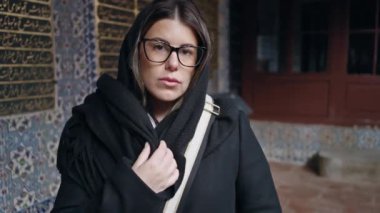 Gözlüklü, gülümseyen genç bir kadın İstanbul 'daki Topkapı Sarayı' nda süslü bir arka planda duruyor. Kültürel tarih ve seyahat duygusunu çağrıştırıyor..