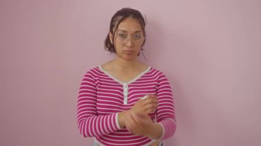 Çizgili tişörtlü kuşkucu genç İspanyol kadın olumsuz bir ifadeyle onaylamıyor. Kendini gergin, kollarını kavuşturmuş, pembe arka planda tek başına dikiliyor..