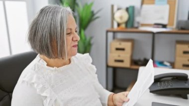 Ofiste doküman okuyan gri saçlı bir kadın. Baş parmak hareketi ile tatmin olduğunu ifade ediyor..