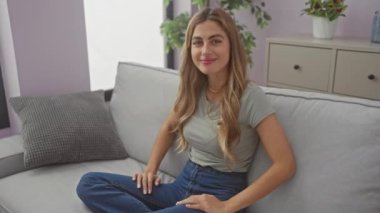 Rahat genç bir kadın, rahat bir oturma odasındaki kanepede neşeyle uzanır. Evde rahatlık ve rahatlık yayar..