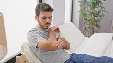 İspanyol adam yatak odasında otururken krem sürüyor.