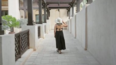 Siyah elbiseli ve beyaz şapkalı bir kadın Dubai 'deki Madinat Jumeirah' ın geleneksel koridorunda geziniyor..