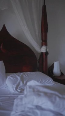 Sakin bir yatak odası, dağınık bir yatak odası, perdeler, ahşap bir yatak başlığı, ve bir yatak başı lambası..