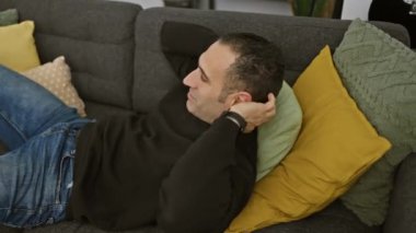 Rahat bir İspanyol adam rahat bir yuva ortamında renkli yastıklarla kanepede uzanıyor.