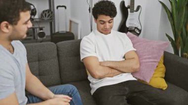 Modern bir oturma odasında gri bir koltukta sohbet eden iki adam.