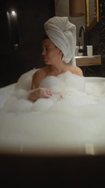 Kafasında havlu olan genç bir kadın lüks bir banyoda köpük banyosunda dinleniyor..