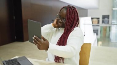 Örgülü, gülümseyen siyah bir kadın modern bir ofiste selfie çekiyor, profesyonel bir iç mekanda neşe sergiliyor..
