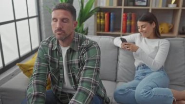 Bir erkek ve bir kadın modern bir oturma odasındaki bir kanepede dinlenirler, kadın akıllı telefonuna odaklanır erkek düşünceli ya da sıkılmış görünürken..
