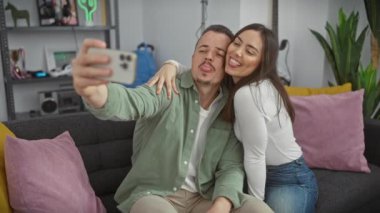 Sıcak bir oturma odasında bir çift selfie çeker. Sevgi dolu anlarını yakalar. Bir kadın, bir erkek ve modern bir iç mekan içerir..