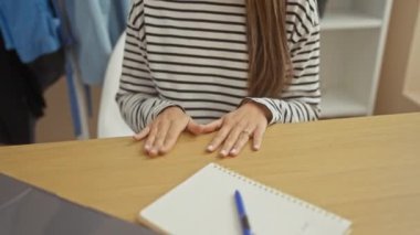 Çizgili tişörtlü İspanyol kadın elinde not defteriyle evde oturuyor, beklenti ve düşünceliliğini ifade ediyor..