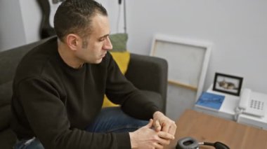 Stresli adam, modern oturma odasında düşünceli bir şekilde oturuyor..