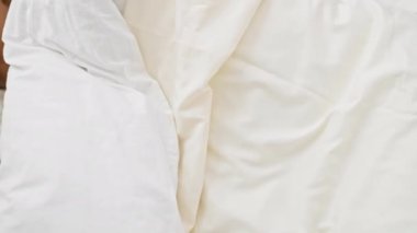 Afro-Amerikalı bir kadın beyaz çarşaflı, parlak, rahat bir yatak odasında huzur içinde uyuyor.