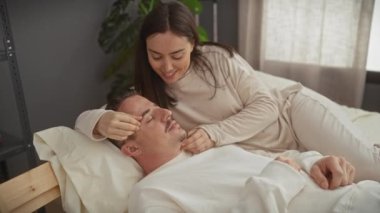 Sevgi dolu bir kadın bir erkeğin alnını okşarken onlar rahat bir yatak odasında dinleniyorlar..