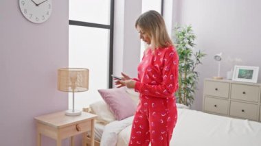 Modern yatak odasında pijamalı beyaz kadın akıllı telefon kullanıyor.