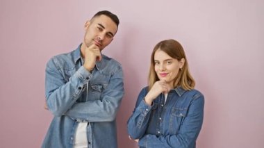 Kendine güvenen, kot gömlekli, uzun boylu, pembe izole edilmiş arka planda kameraya bakan, çapraz kollu, çeneli, pozitiflik saçan güzel bir çift..