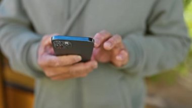 Parkta akıllı telefon kullanan kıdemli bir adam seçici bir şekilde cihaza odaklanıyor..