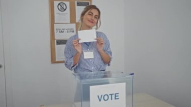 Gülümseyen genç sarışın bir kadın kapalı bir oy verme merkezinde oy kullanıyor. Demokrasi ve vatandaşlık görevini somutlaştırıyor..