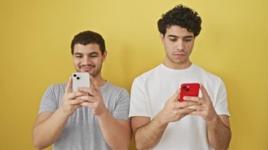 İki adam sarı arka plan bağlantısı ve arkadaşlığı göstermek için akıllı telefonları yan yana kullanıyor..