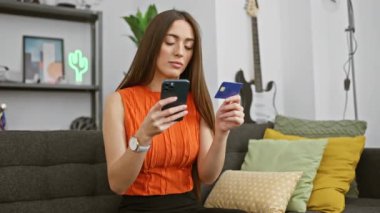 Bir kadın kredi kartını modern oturma odasındaki akıllı telefon uygulaması ile karşılaştırır. İnternet üzerinden alışveriş ya da bankacılık....