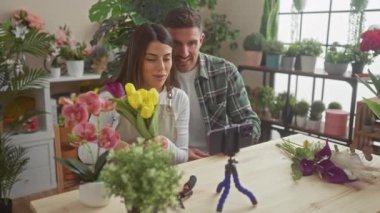 Erkek ve kadın çiçekçide çiçek düzenlerken video kaydı yapıyorlar..