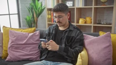 Rahat bir İspanyol adam akıllı telefonuyla meşgul olur, rahat bir oturma odasındaki kanepede oturur..