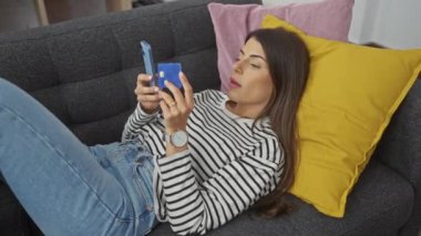 İspanyol kadın rahat bir evde cep telefonu ve kredi kartıyla kanepede yatıyor..