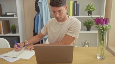 Evdeki ofiste dizüstü bilgisayarı ve çiçekleri olan yakışıklı İspanyol yazar.