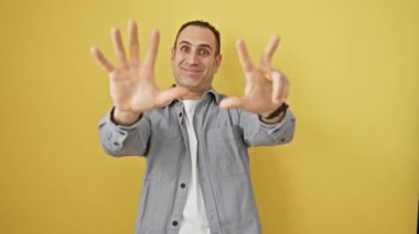 Tişörtlü neşeli, genç İspanyol bir adam, sekiz parmağıyla güvenle işaret ediyor, parlak sarı arka planda izole edilmiş mutlu ve kendinden emin bir ifade gösteriyor..
