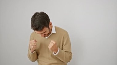 Mest olmuş, süveterli genç adam zaferi sevinçli bir zafer jesti ile kutluyor, izole edilmiş beyaz arka planda başarıyla bağırıyor.