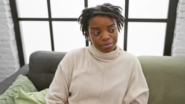 Rasta bukleli genç bir kadın, evdeki kanepede dinleniyor, ateşli dedikoduları dinliyor, daha iyi duyabilmek için elini sıkıyor. Sağırlık onun gösterisine yağmur gibi yağmayacak.