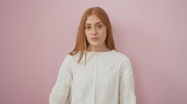 Süveter giyen neşeli, genç, kızıl saçlı bir kadın. Gözleri hoş bir sürprizle kaplıyor. İzole edilmiş pembe arka plana karşı duruyor.