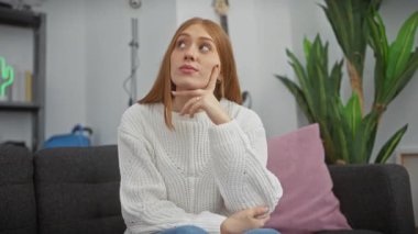 İlgi çekici genç kızıl saçlı kadın, çenesinde parmak, derin düşüncelere dalmış, yukarı bakıyor, şüpheyle delik deşik olmuş, merak ediyor sıcak evinin içinde konsantre olmuş bir an..