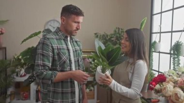 Erkek ve kadın çiçek aranjmanları ve yeşilliklerle çevrili bir çiçekçi dükkanında bitki seçiyorlar..