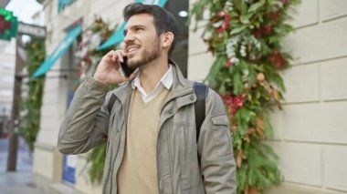 Sakallı genç bir İspanyol, şehir caddesinde yürürken cep telefonuyla konuşuyor. Sıradan ve nişanlı görünüyor..