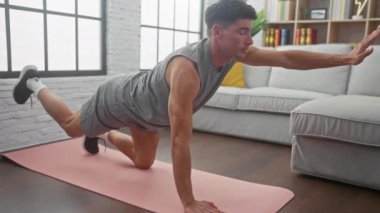 Evde egzersiz yapan İspanyol bir adam oturma odasındaki yoga minderinde kalas kullanıyor..