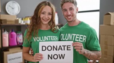 Gülümseyen bir kadın ve yeşil gönüllü gömlekli bir adam bir depoda bağış kutularıyla birlikte 