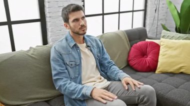 Modern bir oturma odasında koltuktan yükselen İspanyol bir adam, ayrılma ya da hareket hissi veriyor.