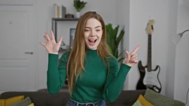 Mutlu genç kadın, kendinden emin ve ışıl ışıl, evde süveter giyiyor, işaret ederken gülümsüyor, yedi numarayı canlı oturma odasında parmaklarıyla gösteriyor..