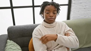 Rastalı genç, kendine güvenen siyah bir kadın, evdeki rahat bir koltukta oturuyor, elini yan tarafa uzatıyor, ciddi bir yüzü olan bir ilan veriyor..