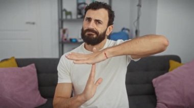 Hayal kırıklığına uğramış orta yaşlı bir adam, kendine güvenen beyaz bir tişört giyiyor, elleriyle bir mola jesti gösteriyor, yüzü ciddi, ev ortamında tartışmalarla dolu..