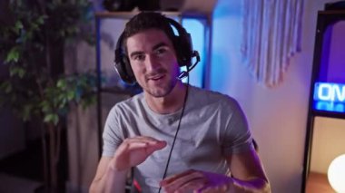 Evdeki modern bir oyun odasında kulaklık takan yakışıklı İspanyol adam geceleri gülümsüyor ve el kol hareketi yapıyor..