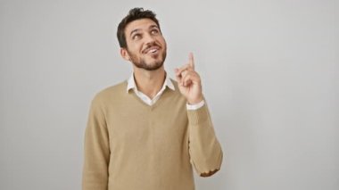 Süveter giyen neşeli, genç, İspanyol bir adam başarılı olur. Zekice bir fikir anında parmağıyla işaret eder. İzole edilmiş beyaz duvarın karşısında duran bu yakışıklı adamın yüzü mutlu bir ifade taşıyor..