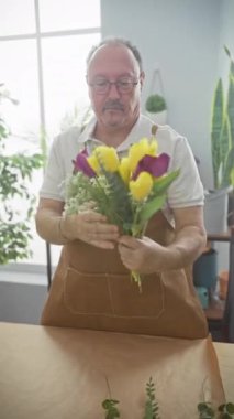 Önlüklü olgun bir adam çiçekçide bir buket lale ayarlıyor.