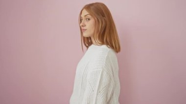 Kendine güvenen kızıl saçlı, doğal bir gülüşü olan, süveter giyen, soyutlanmış pembe arka planda duran genç bir kadın. profil pozu Yakalayıcı tavır, moda ve cazibe