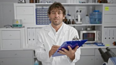 Yakışıklı, sakallı, yeşil gözlü laboratuvar önlüğü giyen, laboratuvar ortamında notlar alan bir İspanyol..